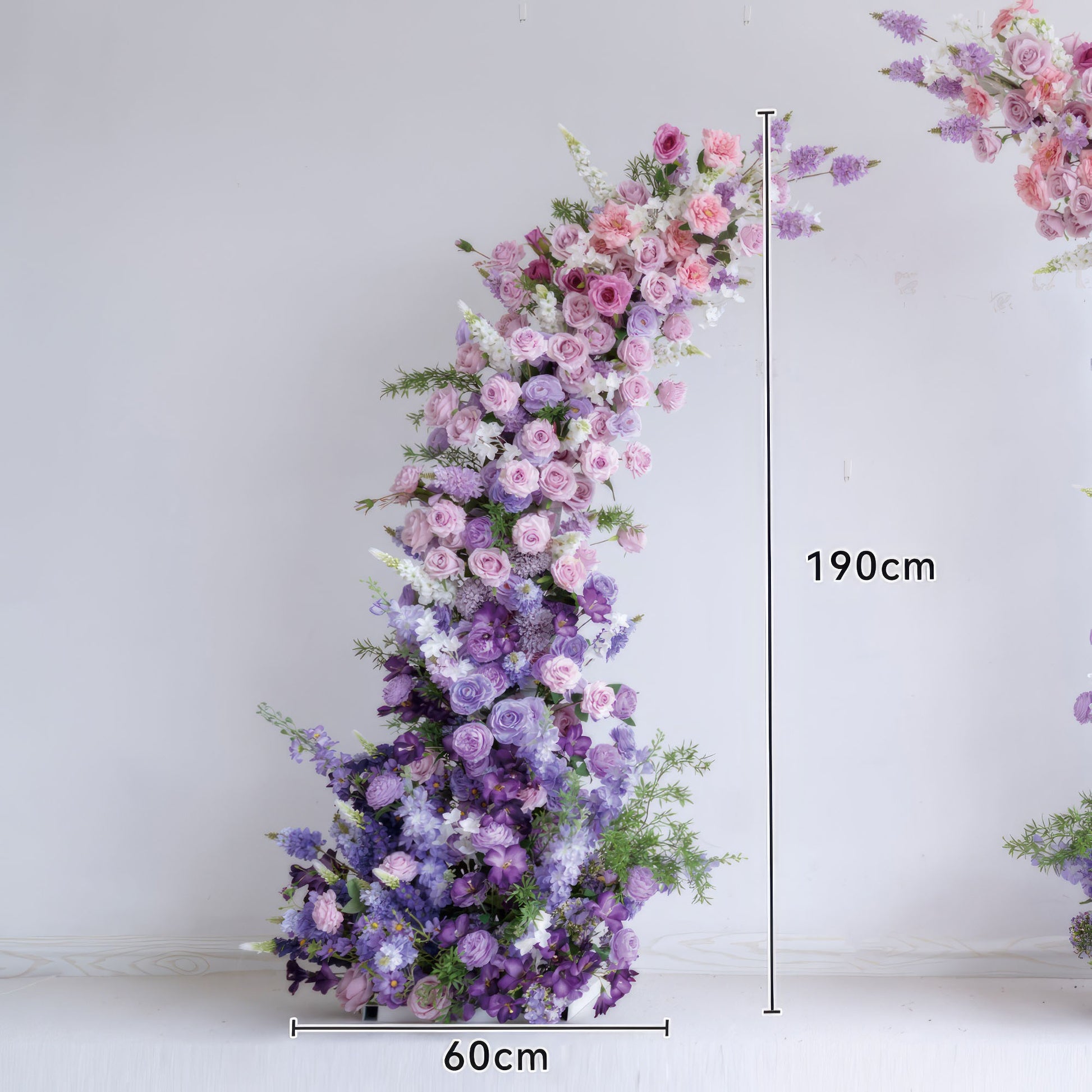This lush floral column from Valar Flowers features a soft gradient of blush pink, lavender, and deep purple blooms—including roses, ranunculus, and hydrangeas—arranged in a cascading, organic shape. Standing 190cm tall, it evokes a romantic, sophisticated atmosphere ideal for weddings, engagement photoshoots, or elegant celebrations.