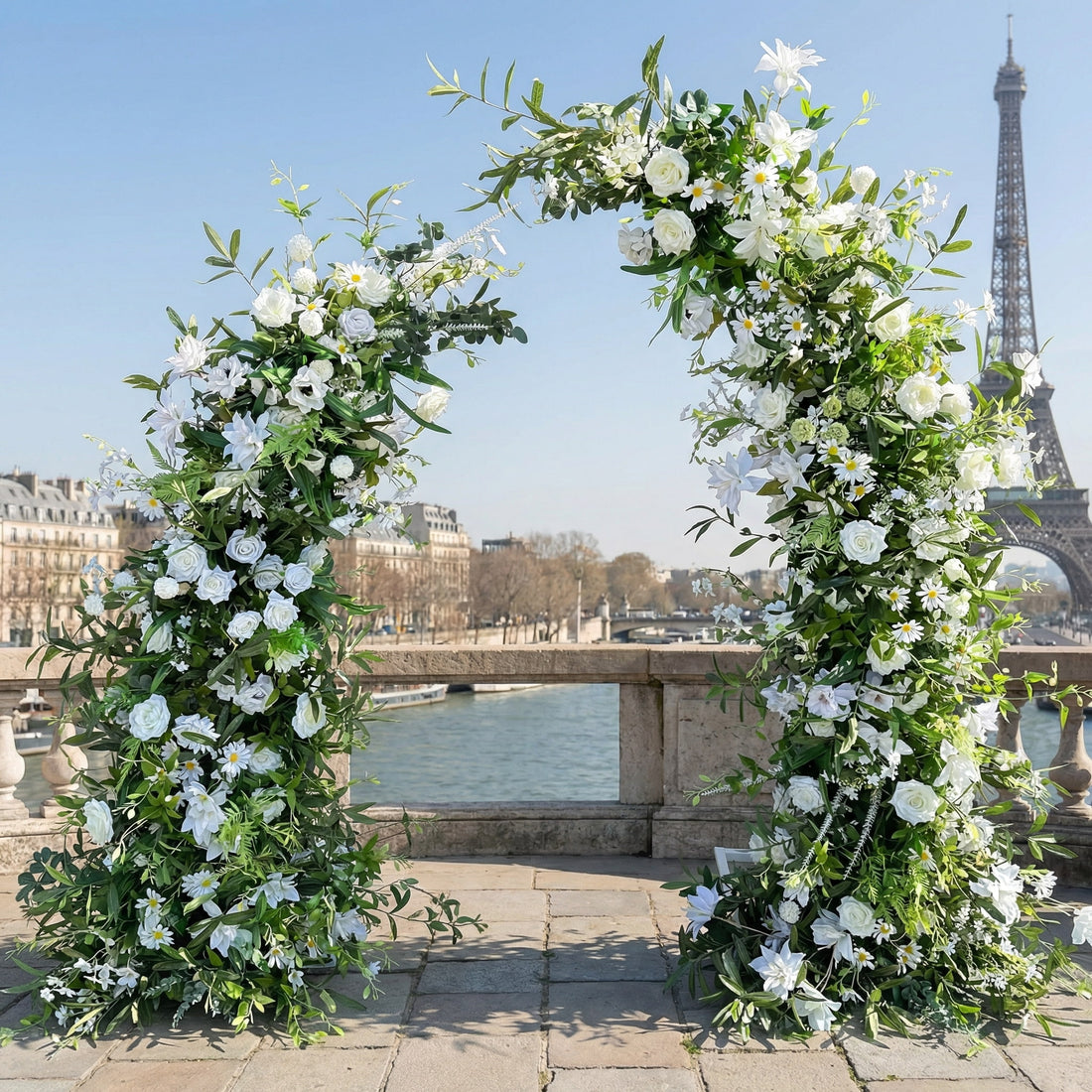 This elegant, asymmetrical floral arch from Valar Flowers is crafted with a fresh palette of crisp white blooms (roses, lilies, daisies) intertwined with lush green eucalyptus and foliage. Set on a sun-dappled Parisian terrace with the iconic Eiffel Tower in the background, it creates a romantic, airy, and sophisticated atmosphere perfect for intimate weddings and refined photoshoots.