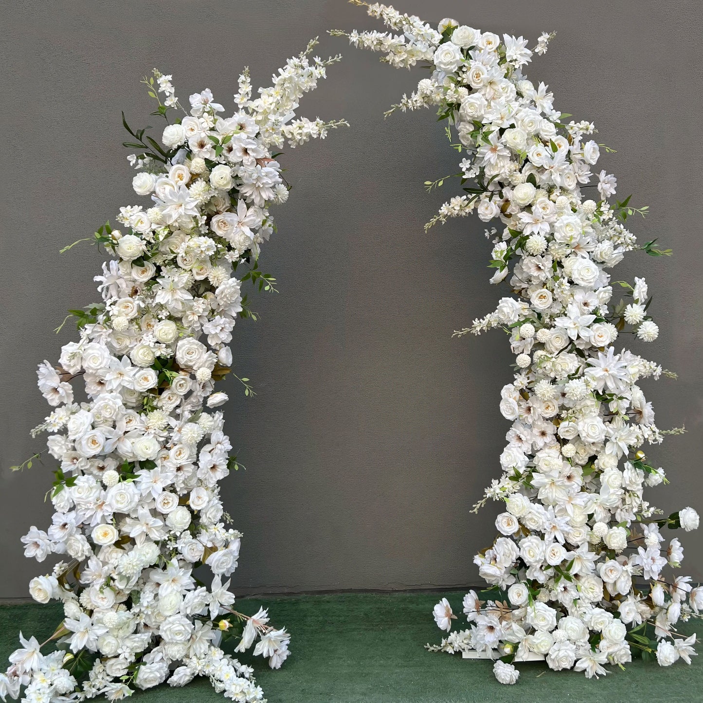 Stunning artificial floral arch for weddings, ceremonies, and special events. Features all-white flowers (roses, lilies, peonies, daisies) with green foliage, arranged in a cascading effect on a sturdy frame. Ideal for indoor/outdoor use. Pure, elegant design enhances any setting.
