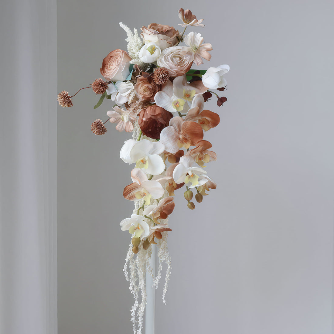This is a cascading floral bouquet featuring a mix of blooms. It includes white and beige orchids, roses, and delicate filler flowers, with earthy - toned spherical blossoms. The flowing design and neutral color palette create an elegant, romantic look, perfect for weddings or special events.