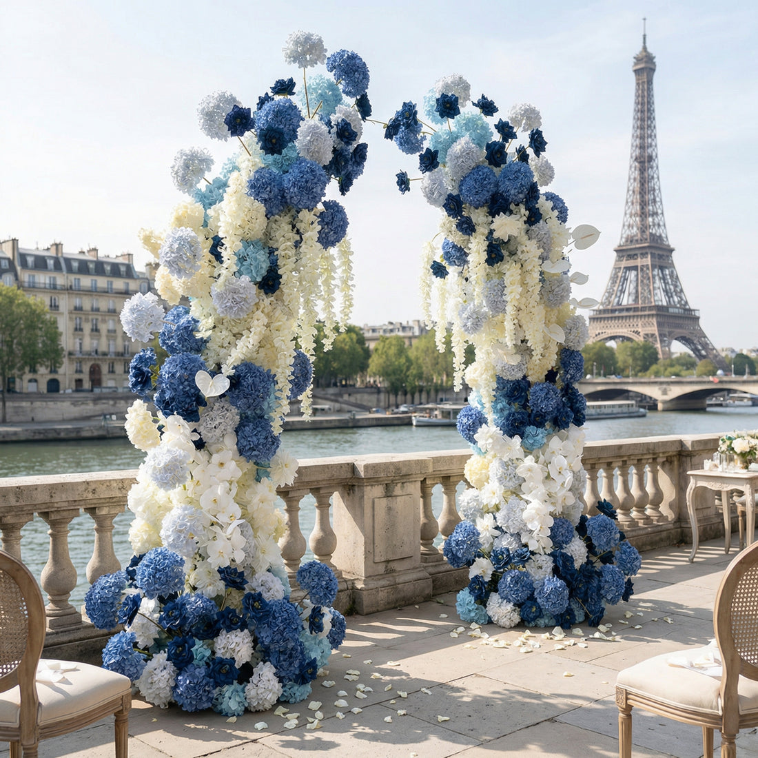 A striking, asymmetrical floral arch from Valar Flowers, crafted with a serene palette of deep navy, sky blue, and creamy white blooms—including hydrangeas, roses, and delicate white anthuriums—intertwined with cascading white foliage. Set against the iconic Eiffel Tower and Seine River in Paris, it creates a sophisticated, unforgettable atmosphere perfect for a luxury wedding or special celebration.