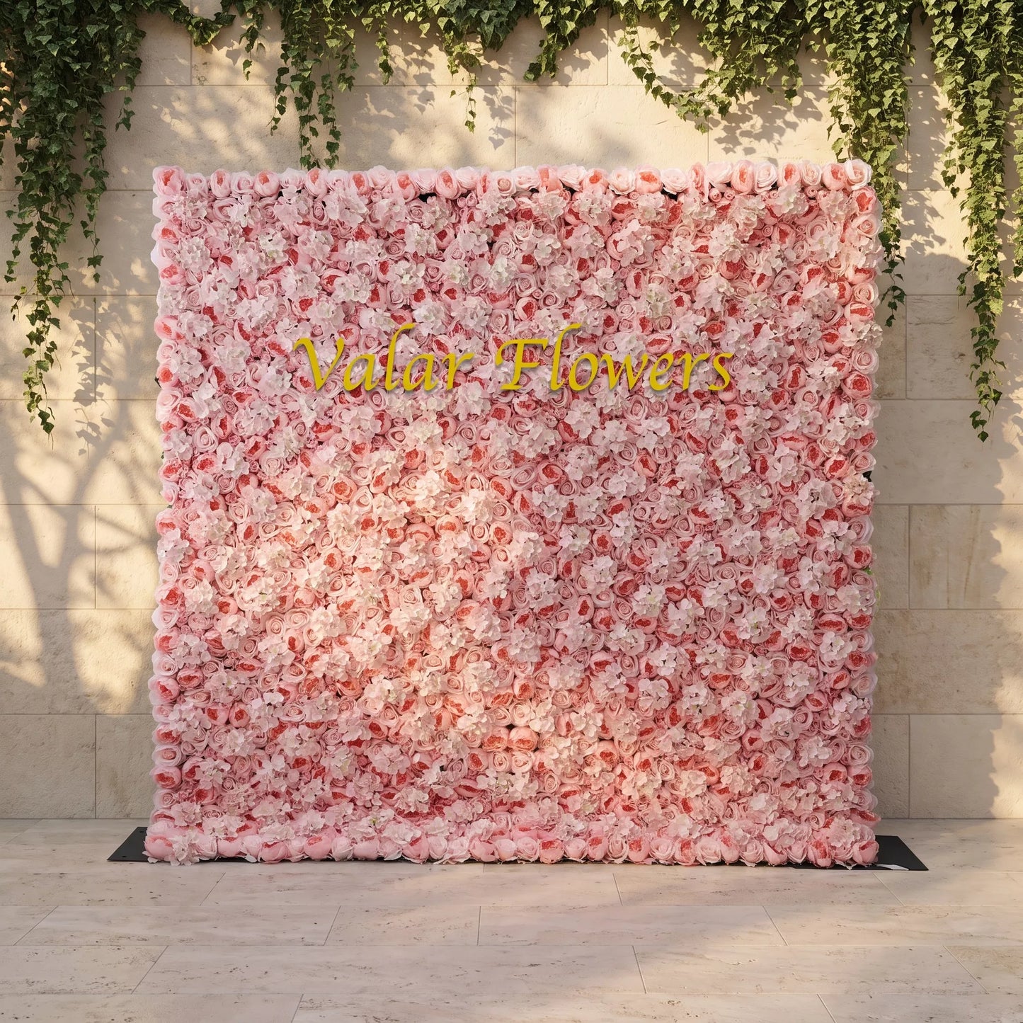 Dense blush pink artificial flower wall layered with soft roses and white hydrangeas, mounted against a stone wall draped with trailing ivy. Bright golden "Valar Flowers" custom branding sits front and center. This reusable, low-maintenance floral backdrop delivers romantic pastel texture, perfect for wedding photo booths, bridal events, boutique store displays and elegant social media content shoots for soft pink-themed celebrations.