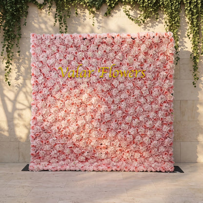 Dense blush pink artificial flower wall layered with soft roses and white hydrangeas, mounted against a stone wall draped with trailing ivy. Bright golden "Valar Flowers" custom branding sits front and center. This reusable, low-maintenance floral backdrop delivers romantic pastel texture, perfect for wedding photo booths, bridal events, boutique store displays and elegant social media content shoots for soft pink-themed celebrations.