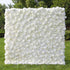 This image showcases a stunning white flower wall by Valar Flowers, composed of dense artificial white roses and blooms. Set outdoors on lush green grass with trees in the background, it exudes elegance and is ideal for events like weddings. The meticulous arrangement highlights Valar Flowers’ craftsmanship in creating sophisticated, eye-catching floral decor.