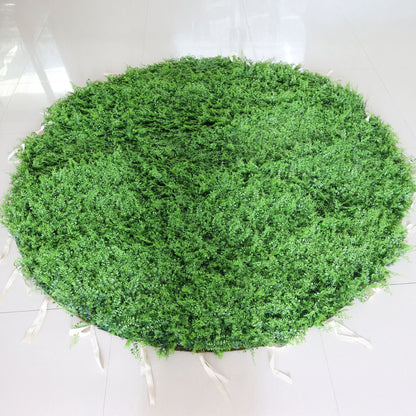This image showcases a round artificial greenery mat by Valar Flowers, placed on a glossy tiled floor. It features dense, lush artificial foliage in a rich green hue, creating a natural and vibrant display. With attached white straps for easy handling, this piece is perfect for adding a touch of organic charm to events or spaces, exuding a fresh and sophisticated atmosphere.