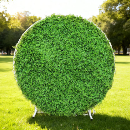 This image showcases a round artificial greenery backdrop by Valar Flowers, set outdoors on a lush green lawn. It features dense, textured green foliage, creating a natural and vibrant display. Bathed in sunlight, this circular piece is perfect for adding a touch of organic elegance to events or photo setups, exuding a serene and sophisticated atmosphere.