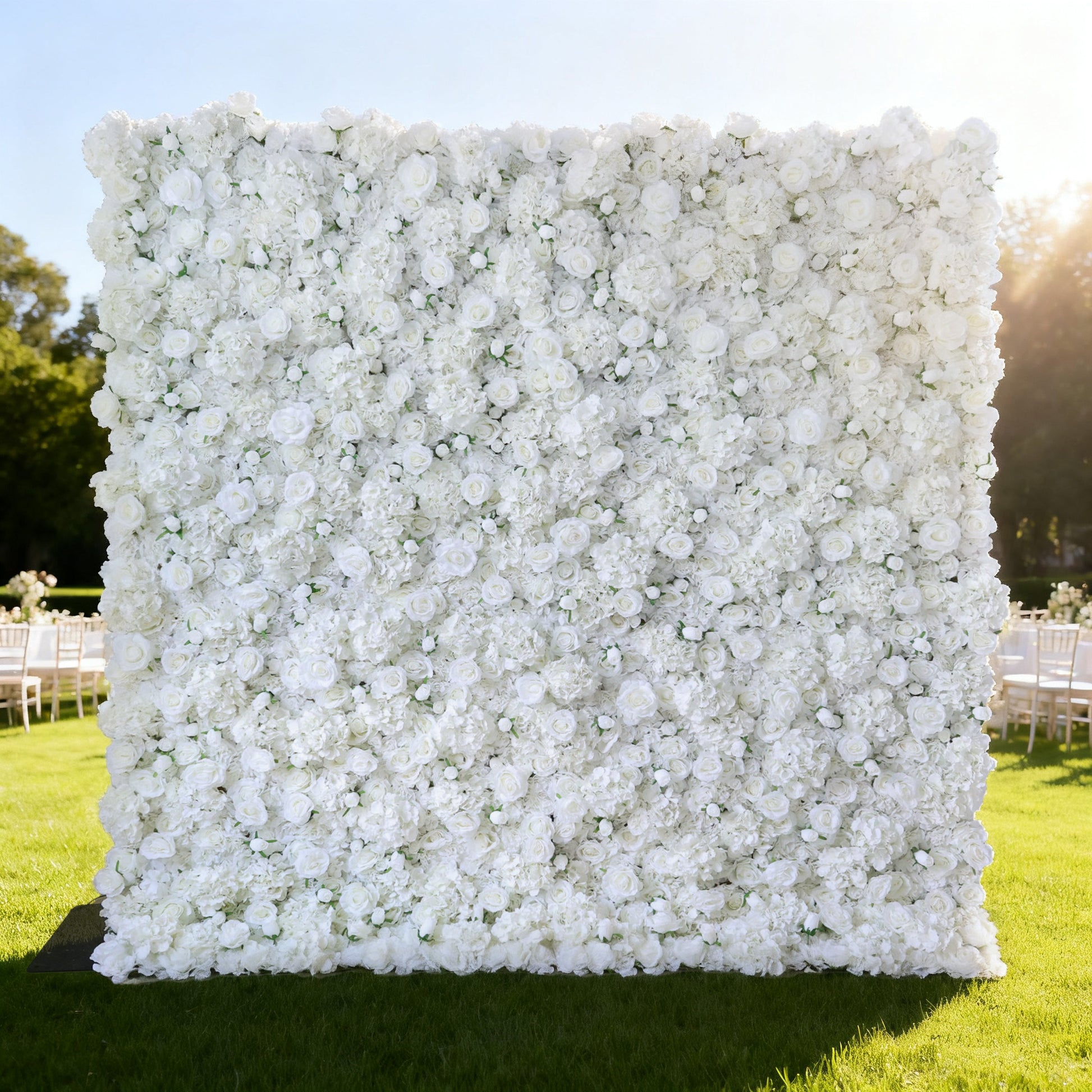This image showcases a large, square floral wall outdoors on a lush green lawn. It's densely covered with pure white flowers, creating a clean, elegant, and serene display. Bathed in sunlight, with trees and event - like setups (white chairs) in the background, the scene exudes a sense of purity, grace, and natural beauty, perfect for decorative purposes in special events or as a captivating backdrop.
