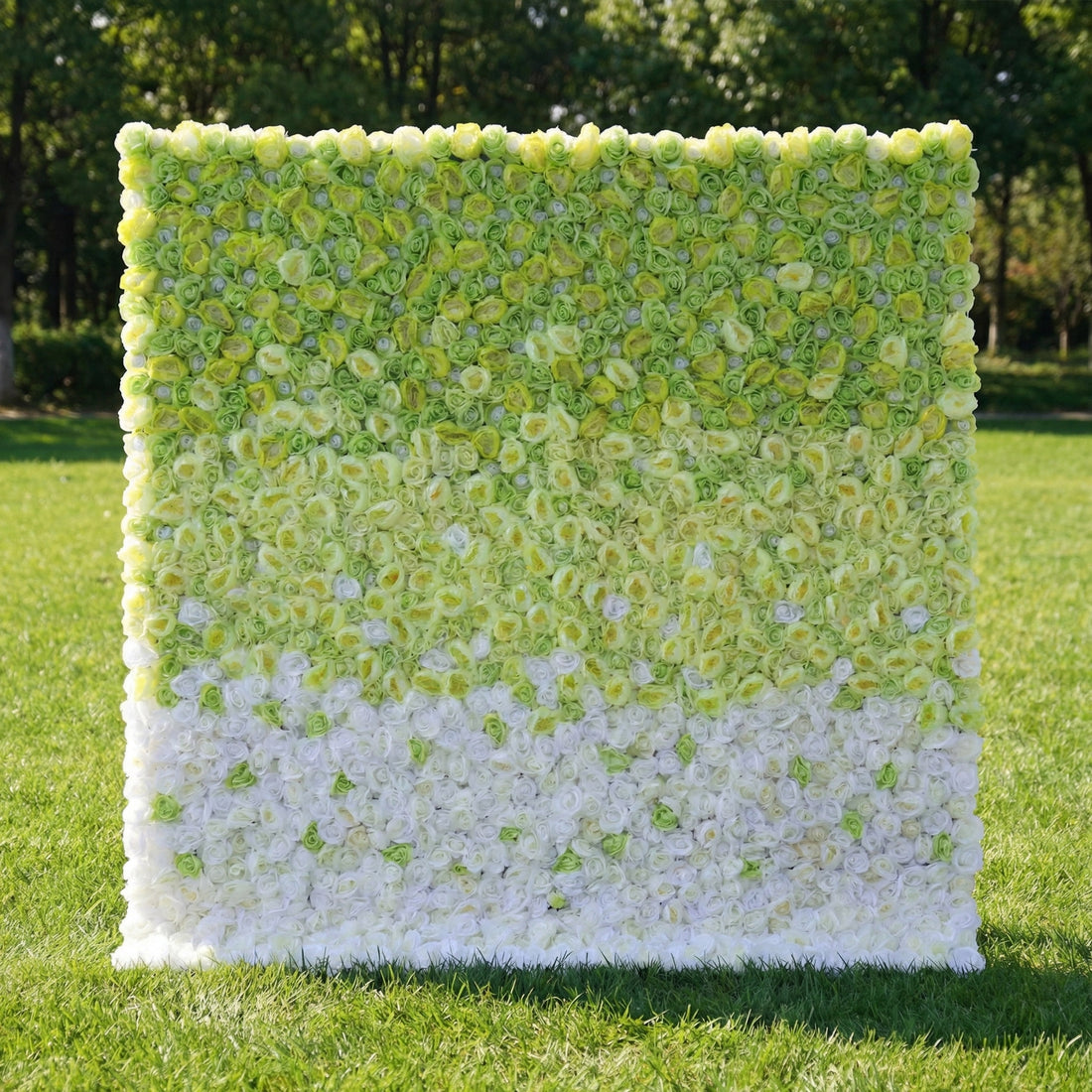 This is a rectangular artificial flower wall backdrop from **Valar Flowers**, featuring a smooth gradient from vibrant green and yellow blooms at the top to soft white flowers at the bottom. Set on a lush green lawn with trees in the background, it creates a fresh, modern, and refreshing aesthetic ideal for photo shoots, weddings, or special outdoor events.