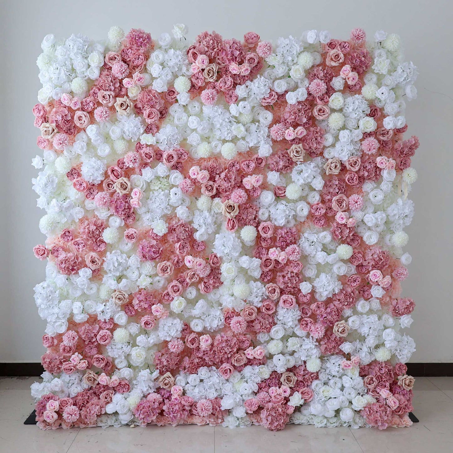 A large floral wall features a captivating mix of white and pink artificial roses and assorted blooms, creating a lush and romantic backdrop. 