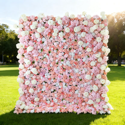 This image showcases a lush floral backdrop by ValarFlowers, set outdoors on a vibrant lawn. It features a dense arrangement of artificial flowers in shades of pink, peach, and white, creating a luxurious, textured display. Bathed in sunlight with a scenic park in the background, it exudes elegance, perfect for adding a nature-inspired, sophisticated element to outdoor events.