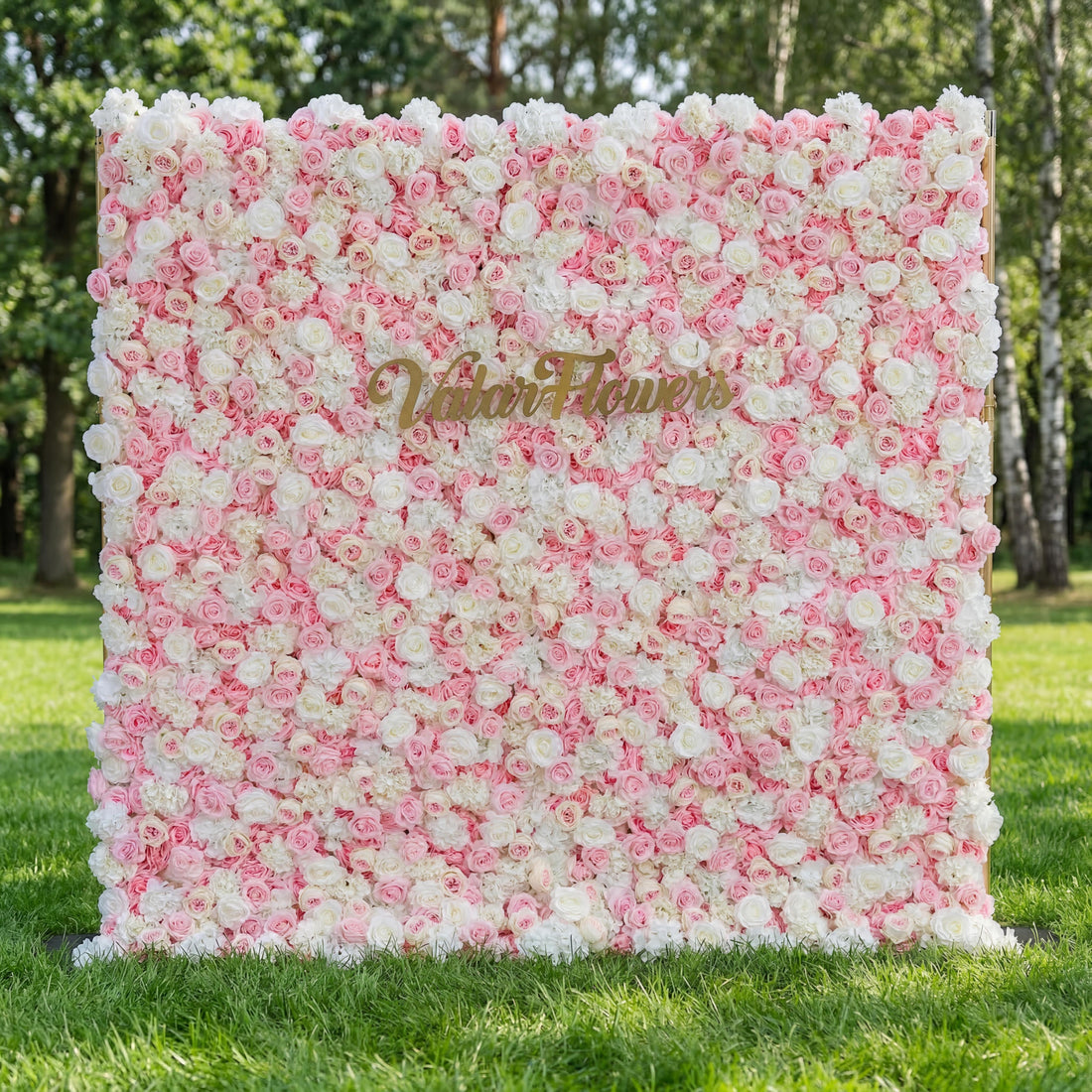 A stunning Valar Flowers floral wall on lush green grass features a dreamy gradient from crisp white at the top to soft blush and deep pink roses. Adorned with a gold "Valar Flowers" script sign, it creates an elegant, romantic backdrop perfect for weddings, bridal showers, and upscale photo sessions