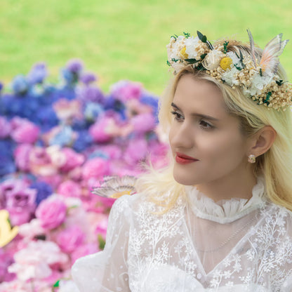 A person with blonde hair wears a floral crown made of white flowers, yellow blooms, and greenery. They&