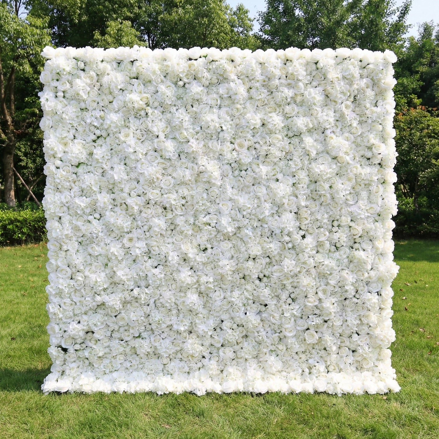 This is a large, rectangular artificial flower wall backdrop from **Valar Flowers**, densely covered with a lush arrangement of white roses, peonies, and small filler flowers. It stands upright on a vibrant green lawn, with a backdrop of leafy trees, creating a clean, elegant, and romantic atmosphere perfect for weddings, photo shoots, or special events.