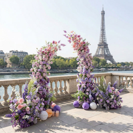 This elegant floral arch from Valar Flowers features a soft pastel palette of blush pink, lavender, and white blooms—including roses, hydrangeas, and delphiniums—arranged in two tall, cascading columns. Set against the iconic Eiffel Tower and the Seine River in Paris, the design evokes a romantic, sophisticated atmosphere ideal for a Parisian wedding or engagement photoshoot.