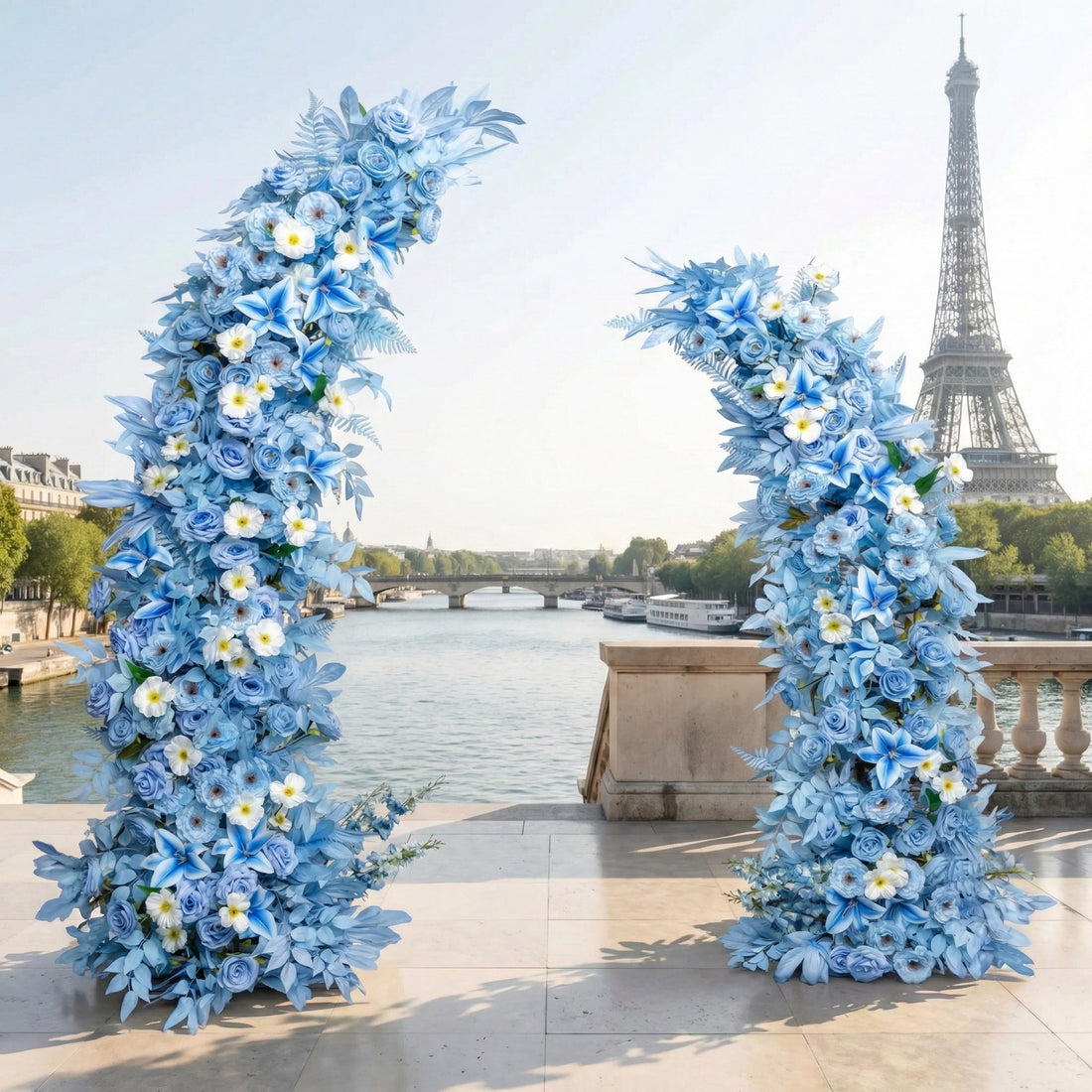 This is a stunning, asymmetrical floral crescent Arch arch from Valar Flowers, crafted with a serene palette of sky-blue roses, lilies, and hydrangeas, accented by delicate white blooms with yellow centers. Set on a Parisian riverside terrace with the iconic Eiffel Tower in the background, it creates a cool, elegant, and dreamy aesthetic ideal for weddings, photo shoots, or special events.
