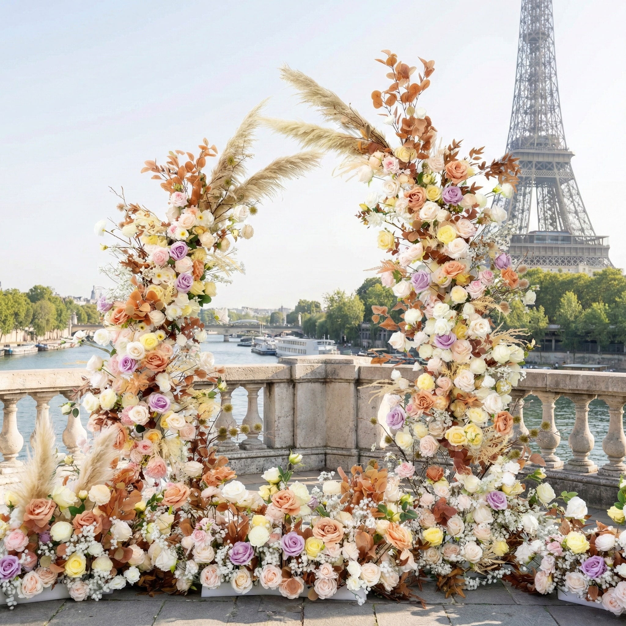 This is a breathtaking, bohemian-style floral arch from Valar Flowers, featuring a luxurious blend of blush pink, cream, terracotta, and lavender blooms, accented with dried pampas grass and eucalyptus. Set on a Parisian stone balcony with the iconic Eiffel Tower and Seine River in the background, it exudes romance, elegance, and rustic charm, perfect for high-end weddings and editorial photoshoots.