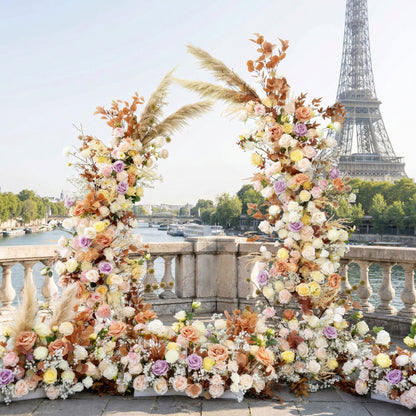 This is a breathtaking, bohemian-style floral arch from Valar Flowers, featuring a luxurious blend of blush pink, cream, terracotta, and lavender blooms, accented with dried pampas grass and eucalyptus. Set on a Parisian stone balcony with the iconic Eiffel Tower and Seine River in the background, it exudes romance, elegance, and rustic charm, perfect for high-end weddings and editorial photoshoots.