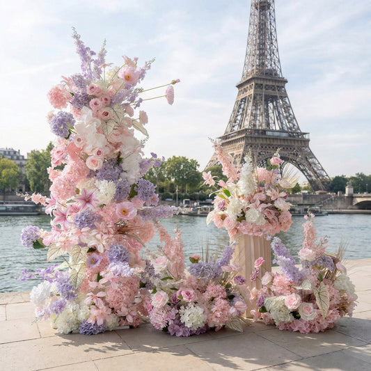 This romantic floral installation from **Valar Flowers** features a dreamy pastel palette of blush pink, lavender, and white blooms—including roses, hydrangeas, and delicate wildflowers—arranged in cascading clusters. Set against the iconic Eiffel Tower and the Seine River in Paris, the design evokes a whimsical, romantic atmosphere ideal for a Parisian wedding, engagement photoshoot, or elegant celebration.
