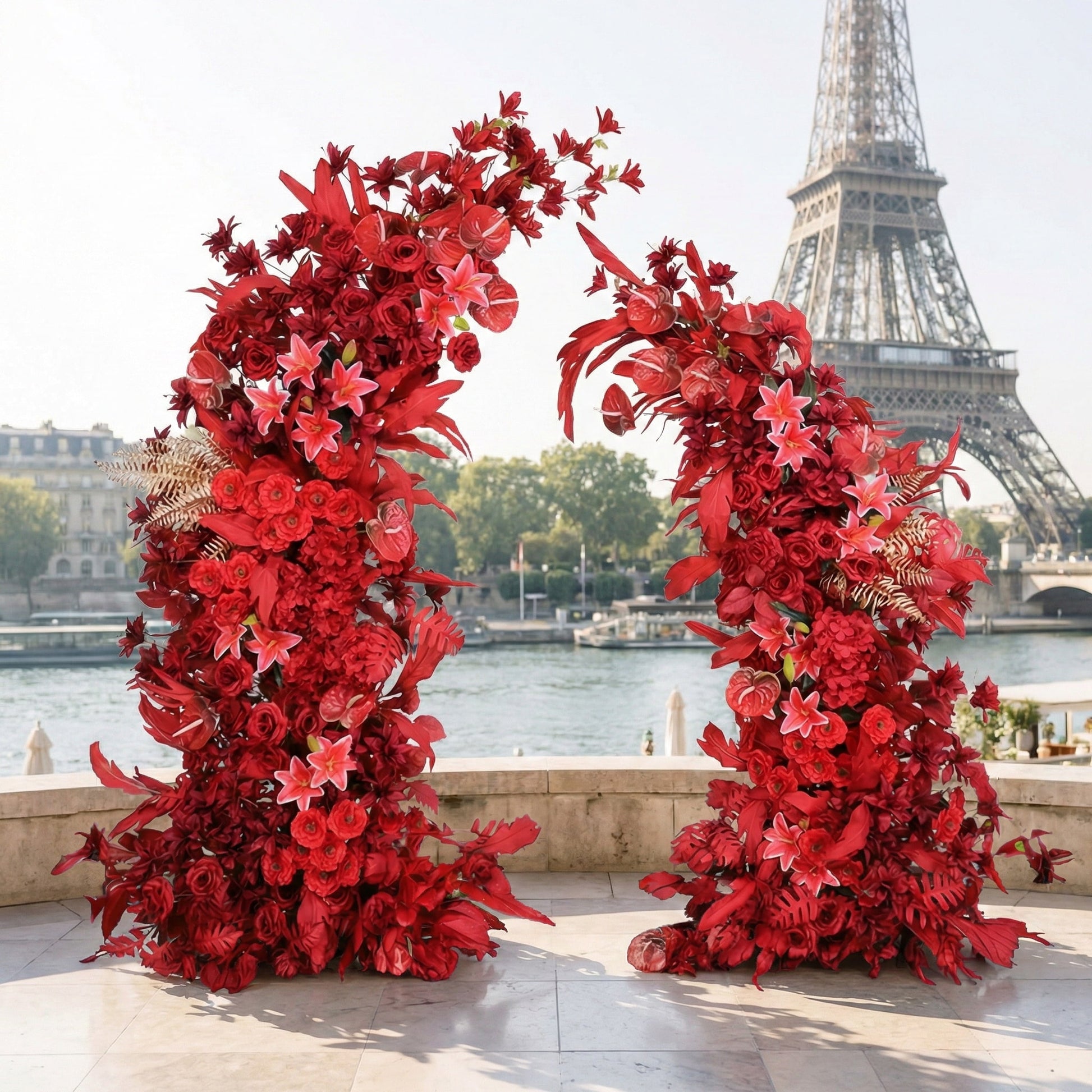 This striking floral arch from Valar Flowers is a bold, cascading arrangement of vibrant red blooms—including roses, lilies, and anthuriums—interwoven with textured foliage and subtle gold accents. Set against the iconic Eiffel Tower and the Seine River in Paris, it creates a dramatic, passionate atmosphere ideal for destination weddings, engagement shoots, or unforgettable celebrations.
