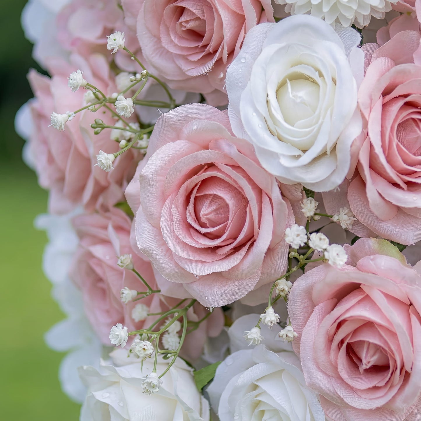 This close-up captures a lush floral arrangement of artificial blush pink and white roses, interspersed with delicate baby's breath. The petals have a soft, satin-like texture, with subtle water droplets adding a fresh, dewy appearance. The dense, layered design creates a romantic, three-dimensional texture, evoking a soft, dreamy atmosphere ideal for weddings, engagement photoshoots, or romantic celebrations.