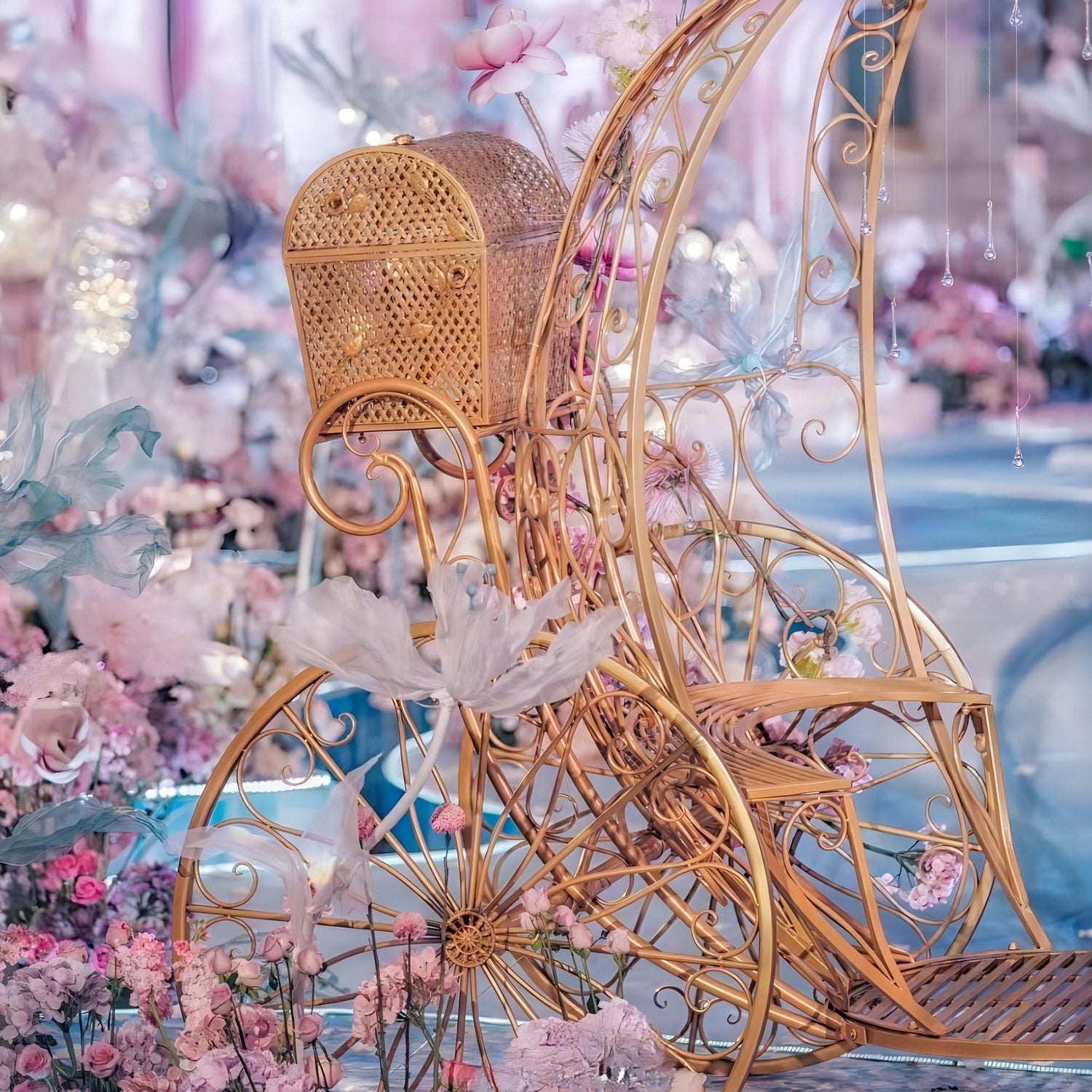 An ornate golden carriage with intricate metalwork and a wicker basket, surrounded by soft pink and white flowers. Ideal for wedding and event decor. ValarFlowers&