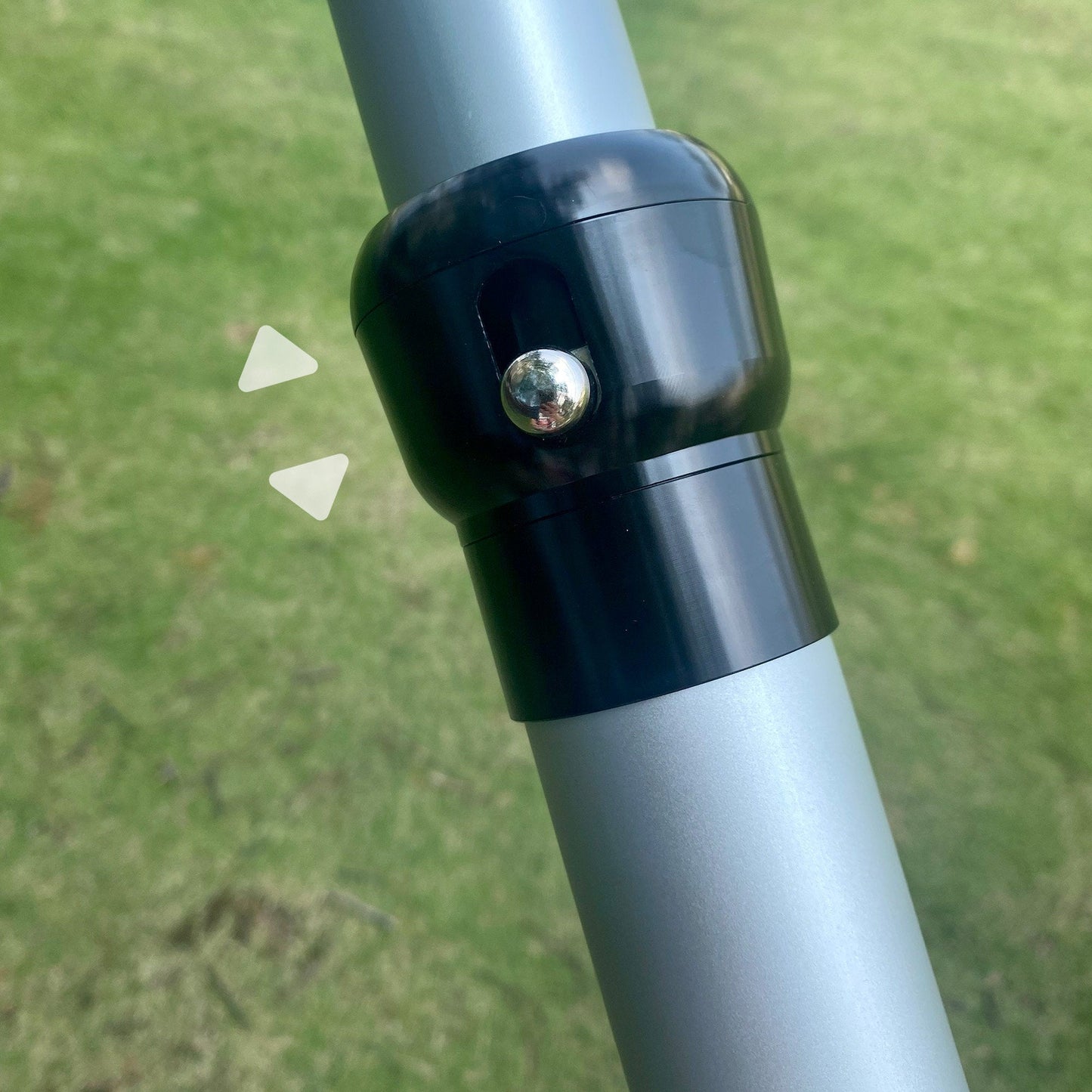 The image shows a close - up of a black connector on a silver metal pole, likely part of a bar system. A metallic knob is visible on the connector, and two white arrow - like shapes point to it, set against a grassy background. 