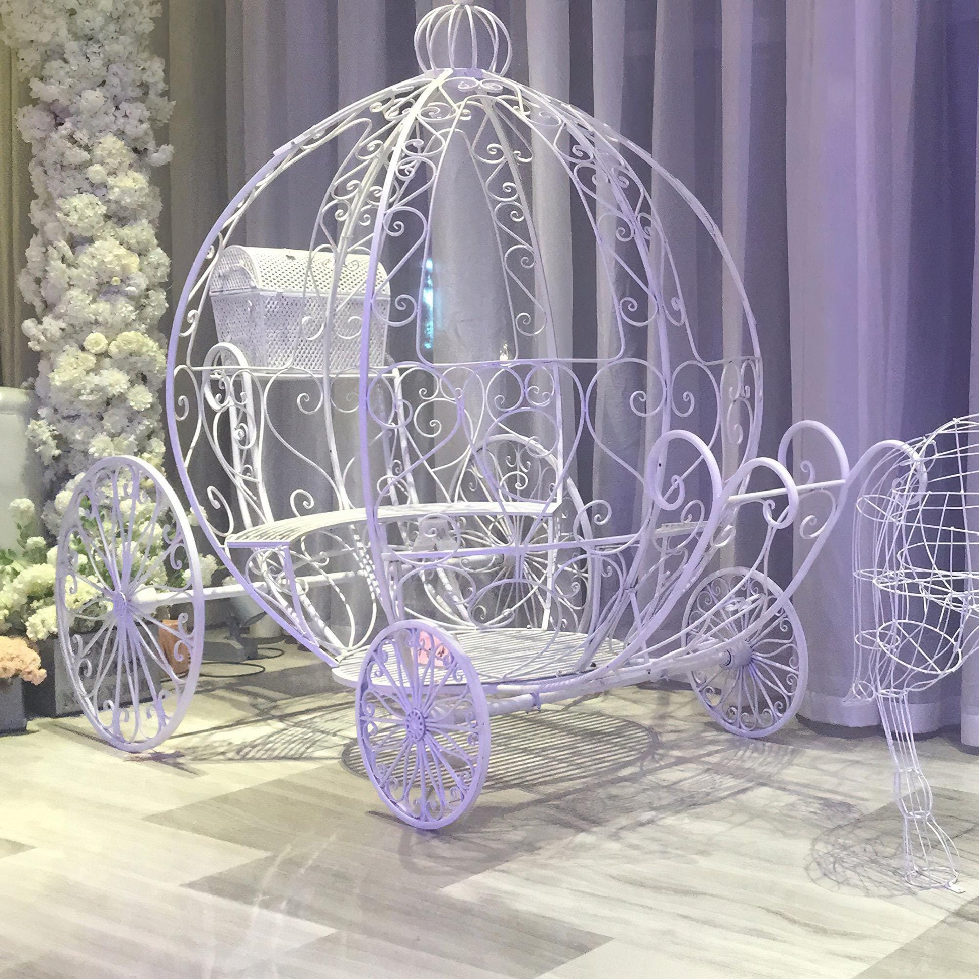 This image by 'ValarFlowers' features a fairytale-inspired white wrought iron carriage with intricate floral designs. It’s ideal for elegant wedding decor, princess-themed events, and unique photo backdrops.