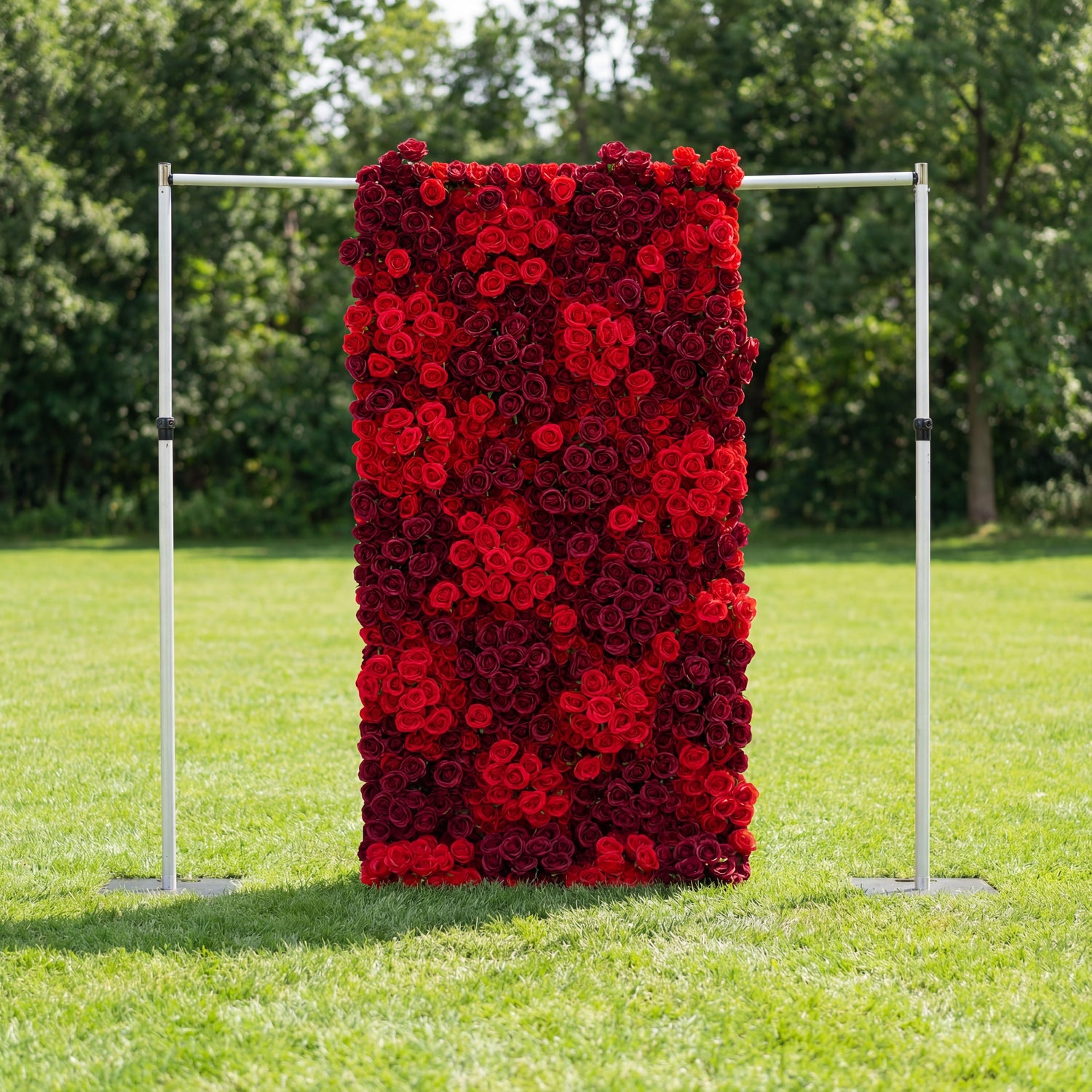 This vertical backdrop (mounted on a sleek silver frame) stands on lush green grass, framed by trees. It’s a dense wall of layered red and burgundy roses, their rich hues creating a romantic, velvety texture. The bold, monochromatic display exudes elegance and passion, making it ideal for outdoor romantic events, proposal setups, or wedding decor.