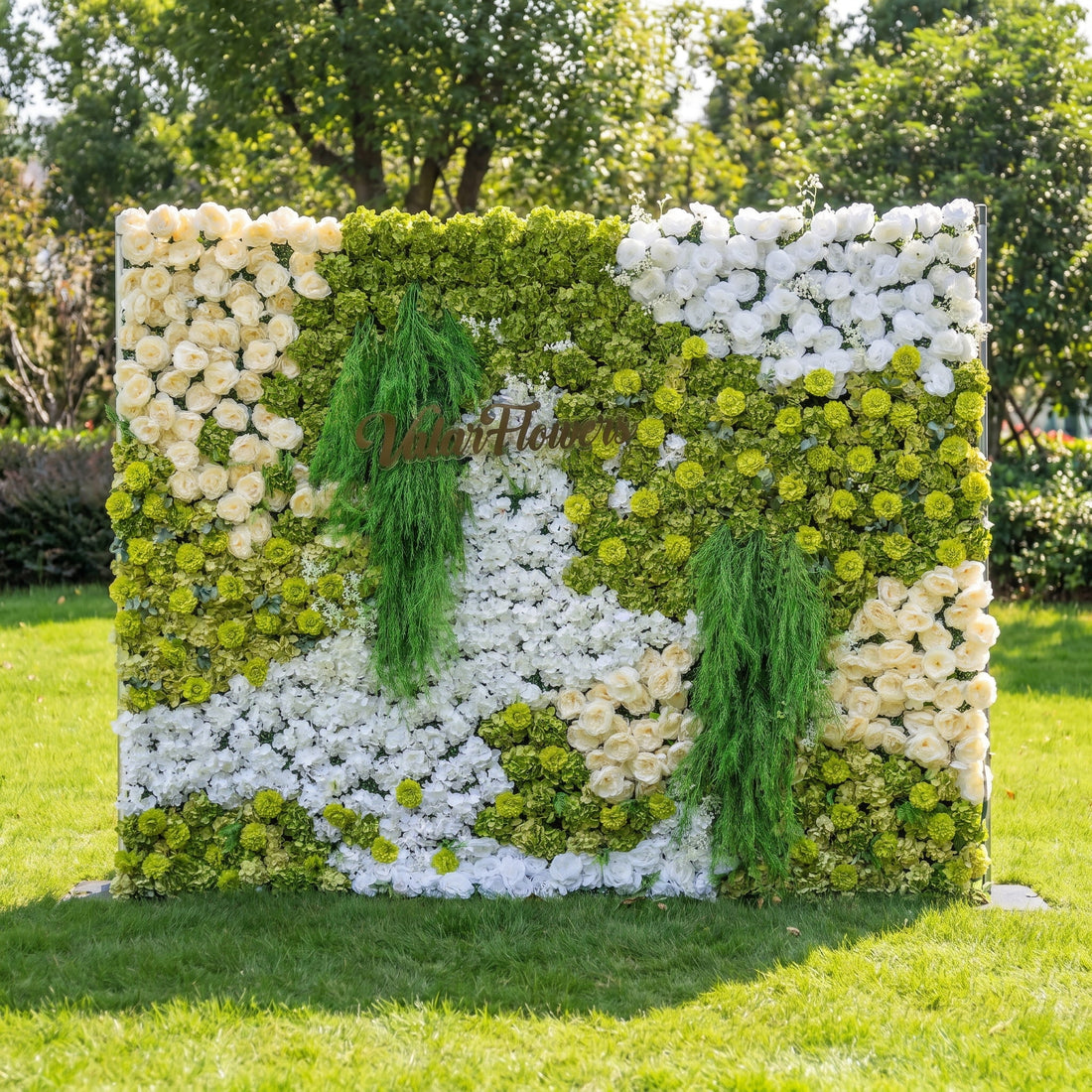 This is a premium green and white artificial flower wall backdrop by Valar Flowers, featuring a lush, nature-inspired design with vibrant green hydrangeas, ivory roses, white blooms, and cascading green foliage. With the brand’s custom logo sign, this reusable, maintenance-free floral display creates a fresh, elegant focal point, ideal for outdoor weddings, garden parties, photo booths, and luxury event styling, offering a long-lasting, nature-themed aesthetic for professional decor.