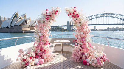 This romantic outdoor floral arch, adorned with a lush gradient of blush pink, deep rose, and white blooms, is set on a luxury yacht with the iconic Sydney Opera House and Harbour Bridge in the background. The arrangement, featuring roses, hydrangeas, and delicate filler flowers, creates a dreamy, three-dimensional texture. Accented with pink and white paper lanterns, it exudes timeless romance, making it the perfect proposal, wedding, or engagement photoshoot focal point.