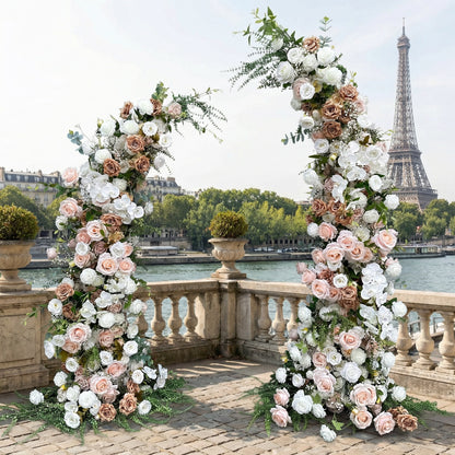 A romantic, asymmetrical floral arch from Valar Flowers, crafted with a soft, warm palette of blush pink, terracotta, and creamy white blooms—including roses and peonies—intertwined with lush greenery. Set on a sunlit Parisian riverside terrace with the iconic Eiffel Tower in the background, it creates a dreamy, elegant, and sophisticated atmosphere perfect for luxury weddings and editorial photoshoots.