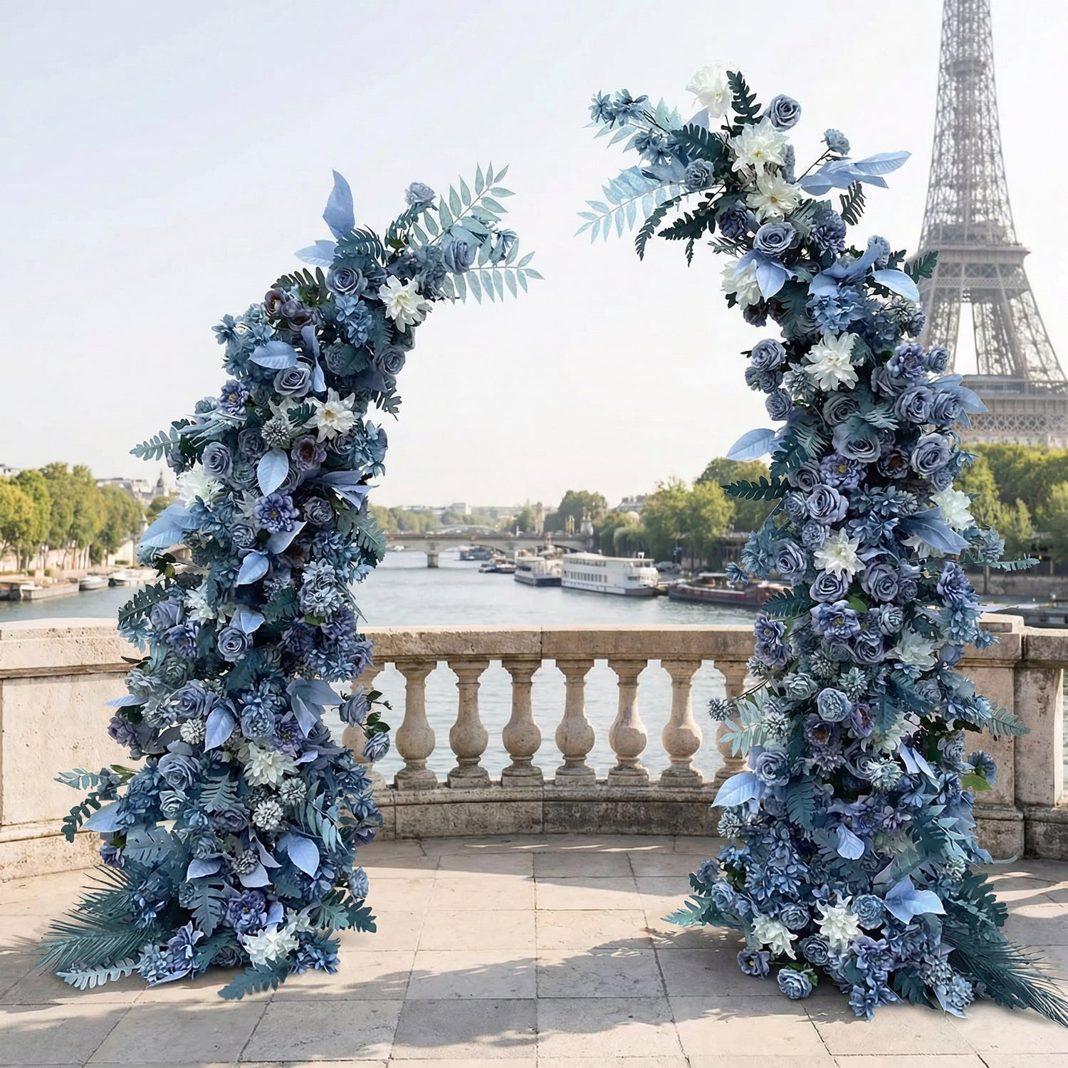 A stunning, asymmetrical floral arch from Valar Flowers, crafted with a cool, serene palette of gradient blue blooms—from deep navy to soft sky blue—intertwined with white accents and textured blue-green foliage. Set on a sunlit Parisian riverside terrace with the iconic Eiffel Tower in the background, it creates a modern, elegant, and ethereal atmosphere perfect for luxury weddings and editorial photoshoots.