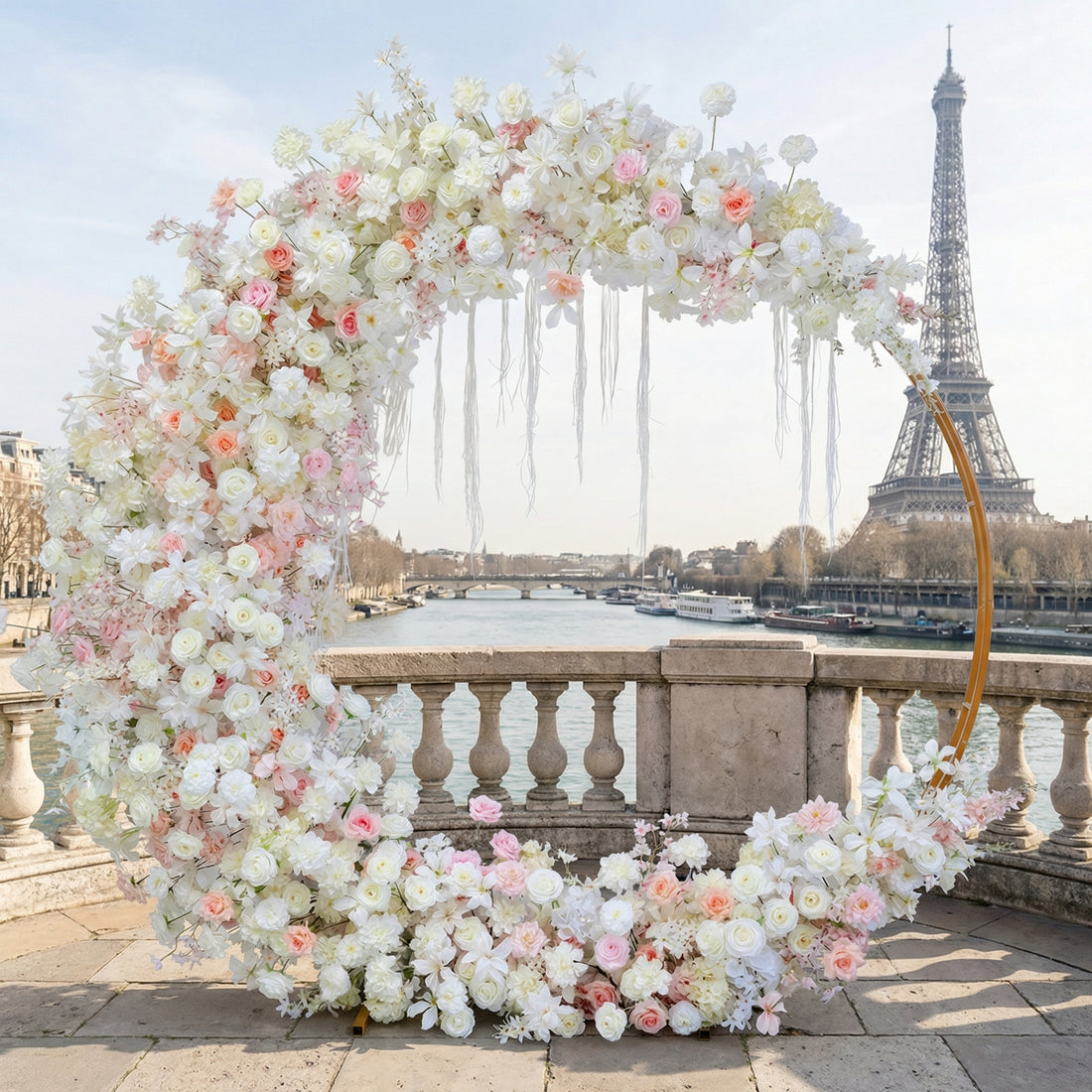 A dreamy, circular floral arch from Valar Flowers, bursting with a soft palette of creamy white, blush pink, and delicate peach blooms—including roses, peonies, and cascading white ribbons—set against the iconic Eiffel Tower in Paris. The lush, romantic design creates an unforgettable atmosphere perfect for a wedding or proposal celebration.