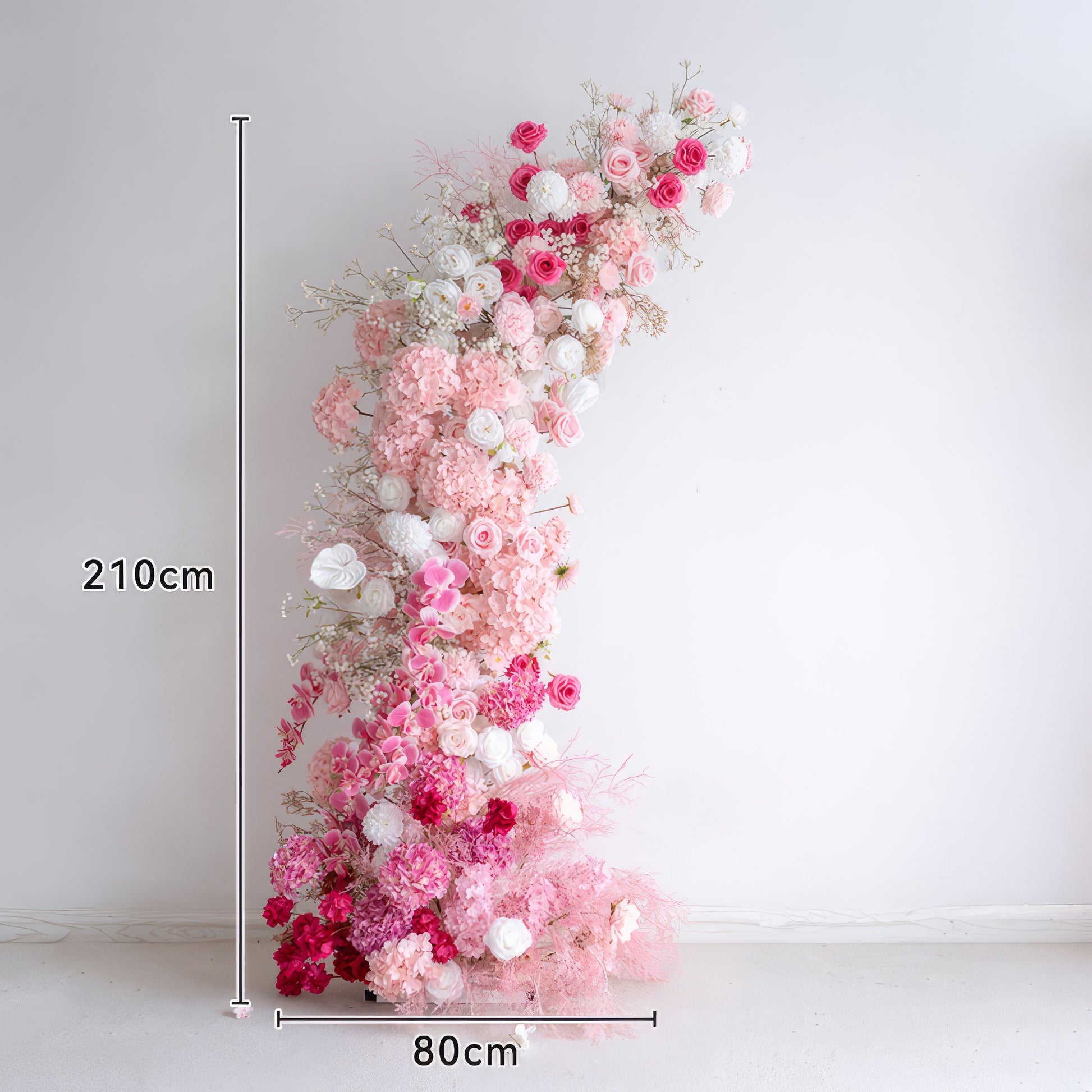 This 210 cm tall, 80cm wide floral arrangement features a romantic gradient of blush pink, deep rose, and white blooms, including hydrangeas, roses, and delicate filler flowers. The lush, cascading design creates a dreamy, three-dimensional texture, making it a stunning focal point for weddings, engagement photoshoots, or romantic celebrations against a minimalist white backdrop.